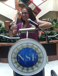 Emily, giving thumbs-up, at podium with NSF logo.